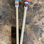 two hairpins with beaded caps, one is rainbown and blue and one is black and red on wooden pins