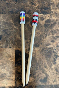 two hairpins with beaded caps, one is rainbown and blue and one is black and red on wooden pins