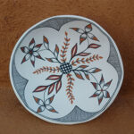 white pottery bowl with hand painted geometric flower design. black and white striped triangles on border surround orangey-red and white flower designs