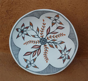 white pottery bowl with hand painted geometric flower design. black and white striped triangles on border surround orangey-red and white flower designs